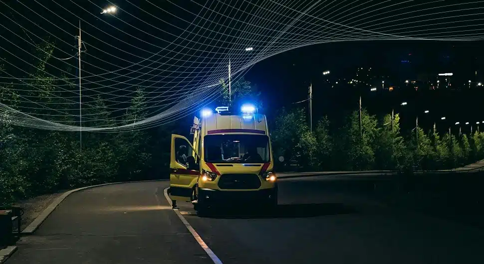 An ambulance with flashing blue lights standing on a road at night.