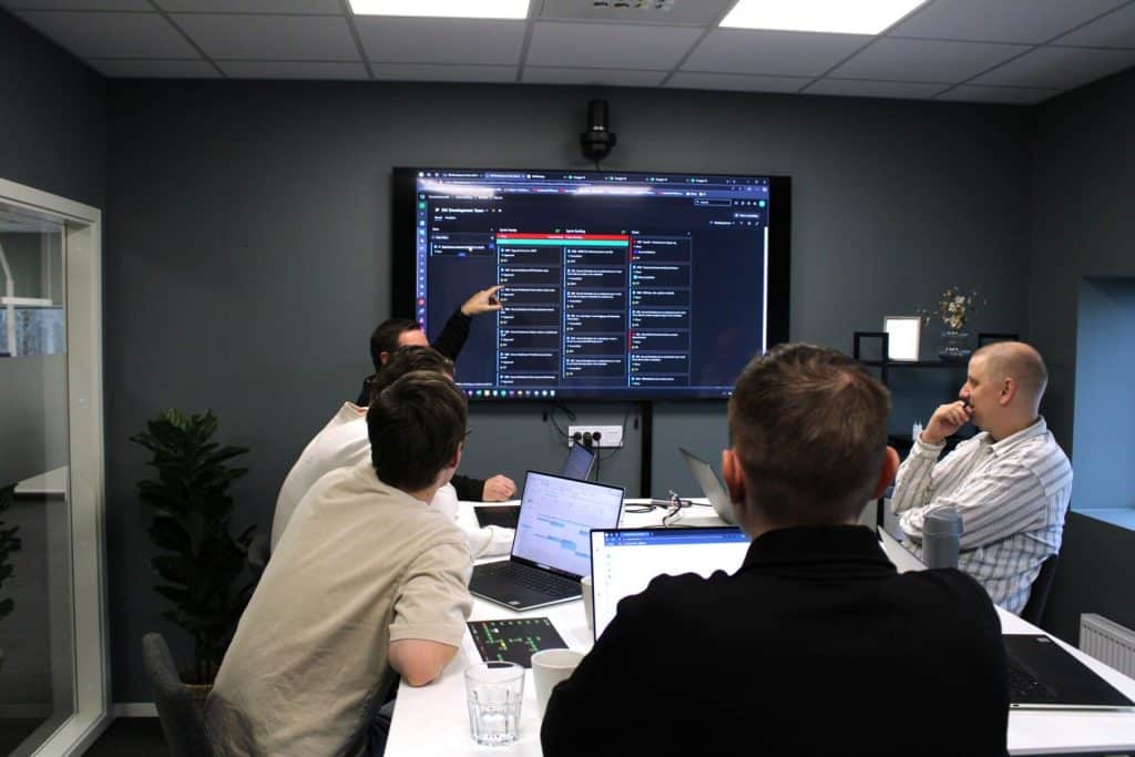 Group of people in a meeting room looking at a large screen with project data.